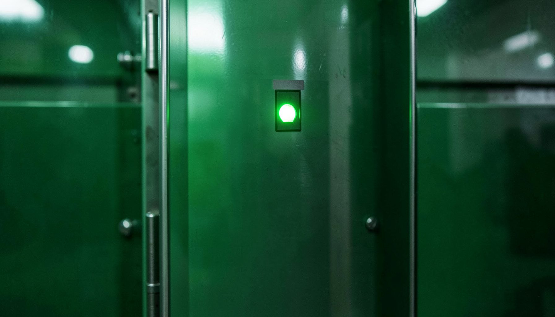 Close-up of a printer control panel with glowing green indicator lights, metallic surfaces reflecting workshop illumination, conveying precision and technical reliability.