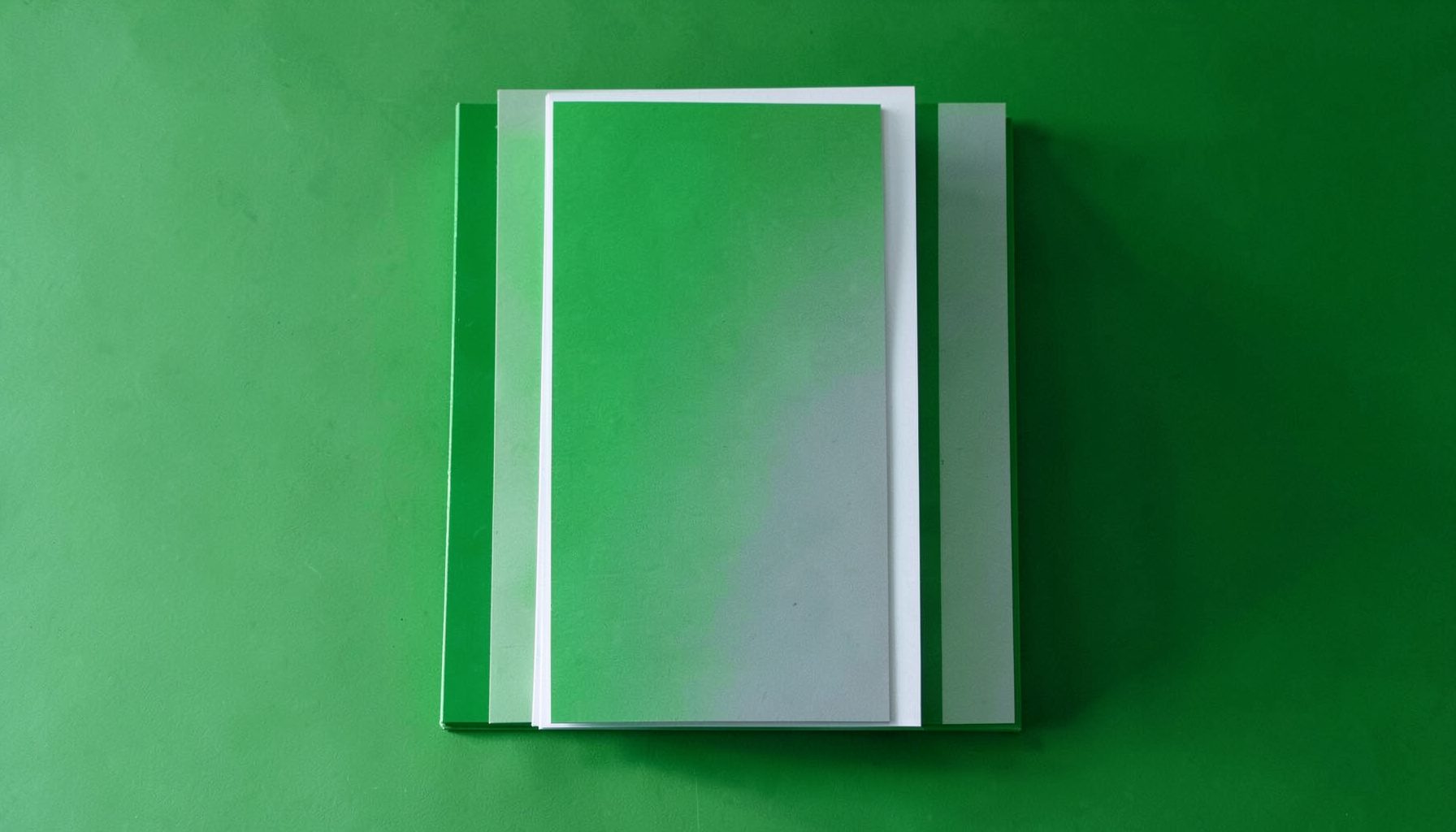 Neatly stacked colorful flyers on coated paper with a soft sheen under natural light, predominantly white, green, and gray.
